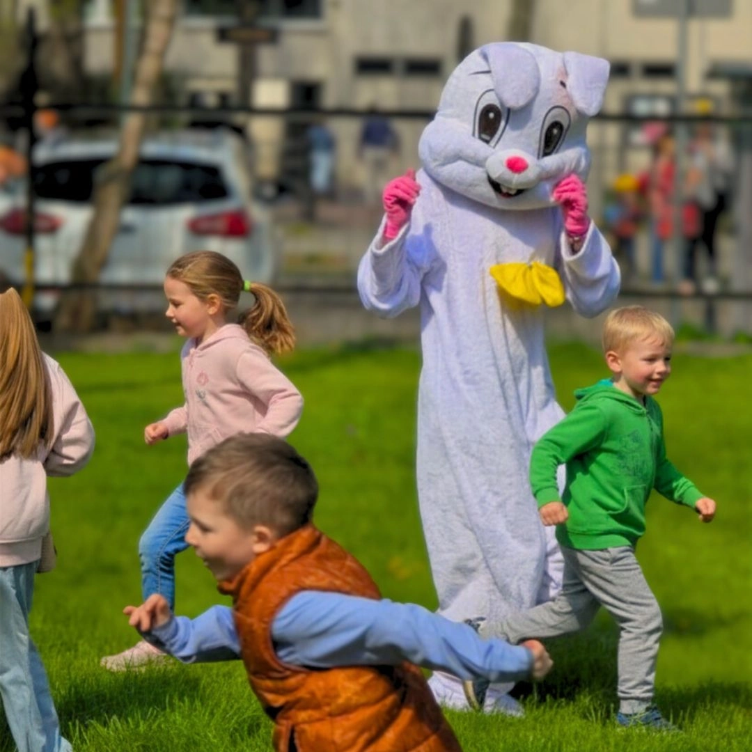 Dzieci bawią się na trawie obok osoby w kostiumie wielkanocnego zająca podczas hotelowych animacji na świeżym powietrzu.