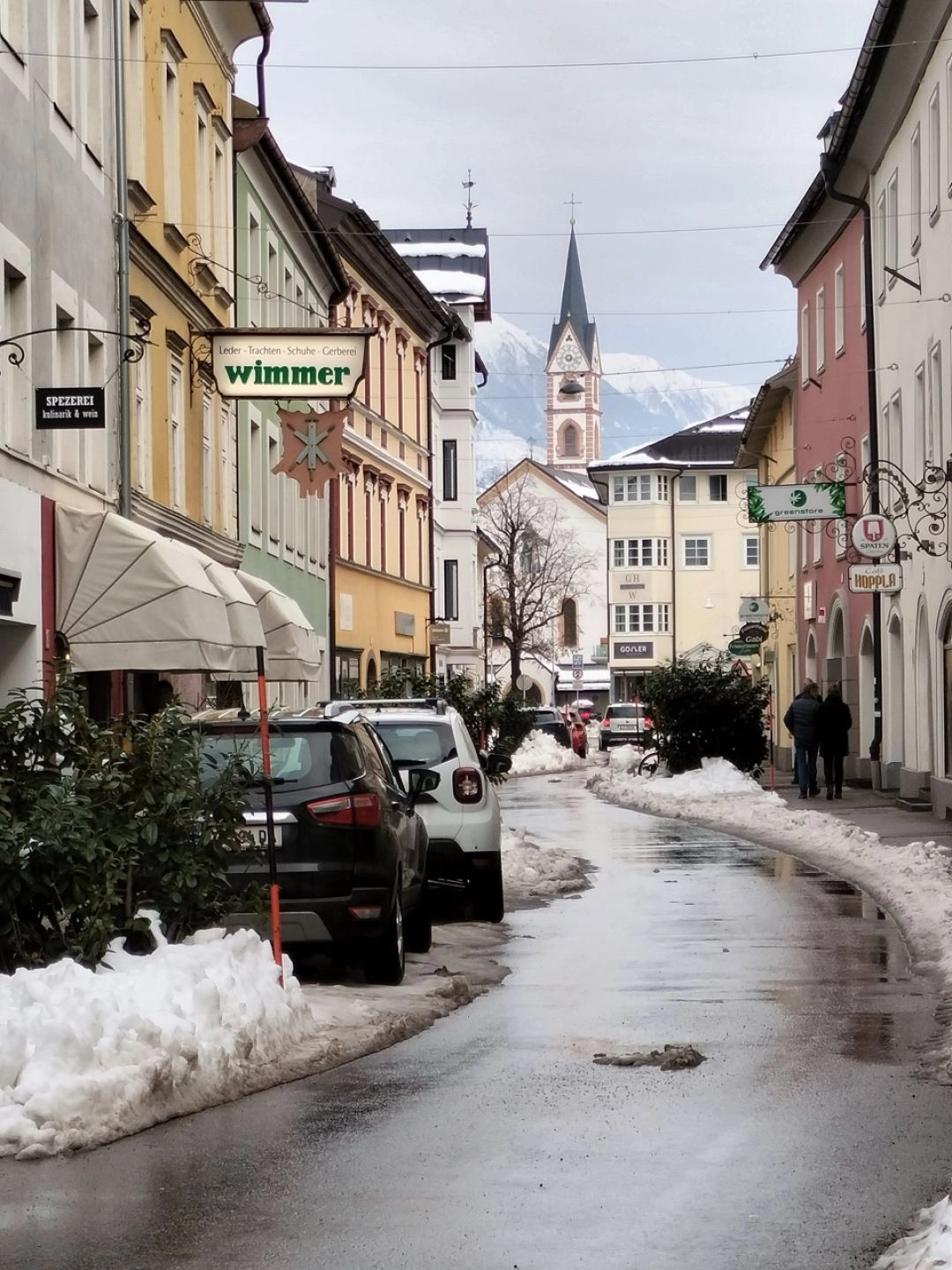Ulica w historycznym centrum Lienz z widokiem na wieżę kościoła i alpejskie góry w tle.