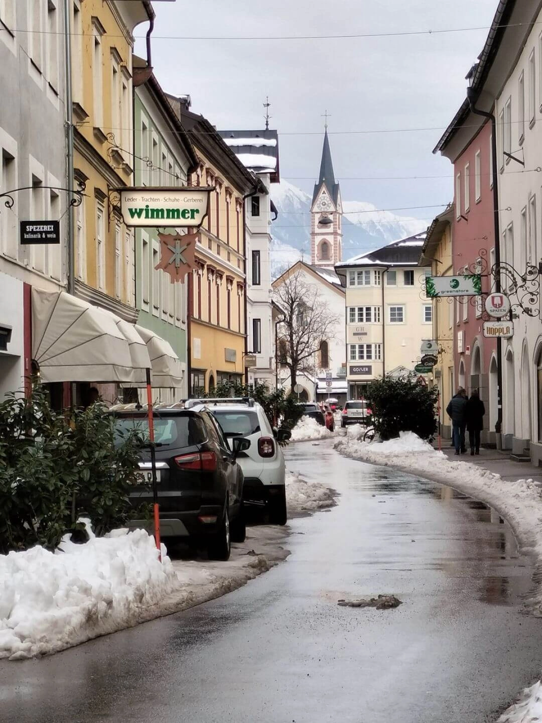 Ulica w historycznym centrum Lienz z widokiem na wieżę kościoła i alpejskie góry w tle.