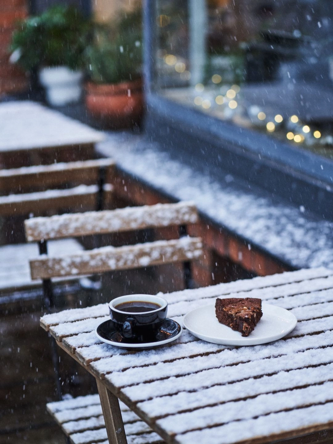 Filiżanka czarnej kawy i kawałek ciasta na zaśnieżonym drewnianym stoliku przed kawiarnią