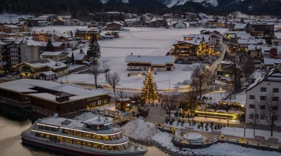 Oświetlony statek na jeziorze Achensee zimą, otoczony górami i świątecznymi dekoracjami, podczas pływającego jarmarku adwentowego.