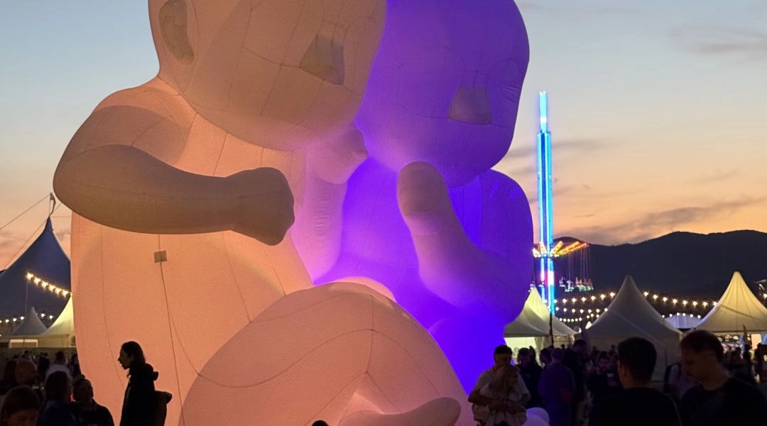 Dwie ogromne, podświetlane dmuchane postacie na terenie festiwalu Pohoda o zachodzie słońca, wśród namiotów i uczestników wydarzenia.