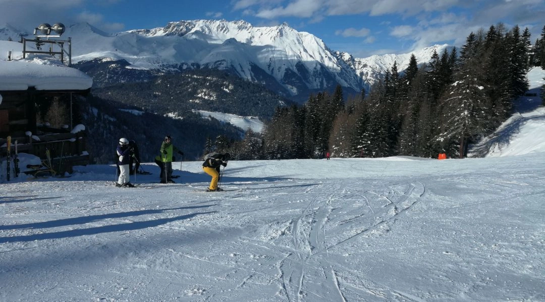 Narciarze na szerokiej trasie w ośrodku Nauders w Tyrolu, w tle ośnieżone alpejskie szczyty.