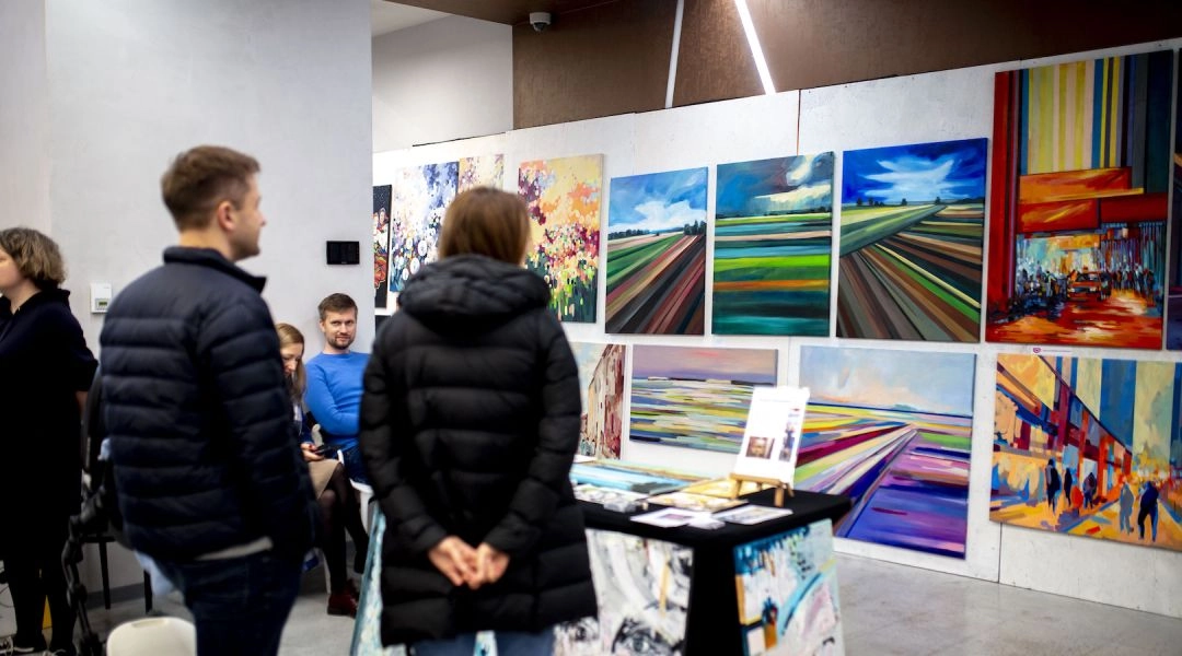 Stoisko z kolorowymi obrazami i odwiedzający podczas Targowiska Sztuki w Warszawie.