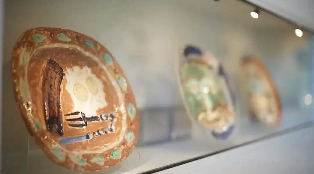 Ceramiczne talerze prezentowane za szkłem w muzealnej gablocie, na pierwszym planie naczynie z charakterystycznym malarskim wzorem.