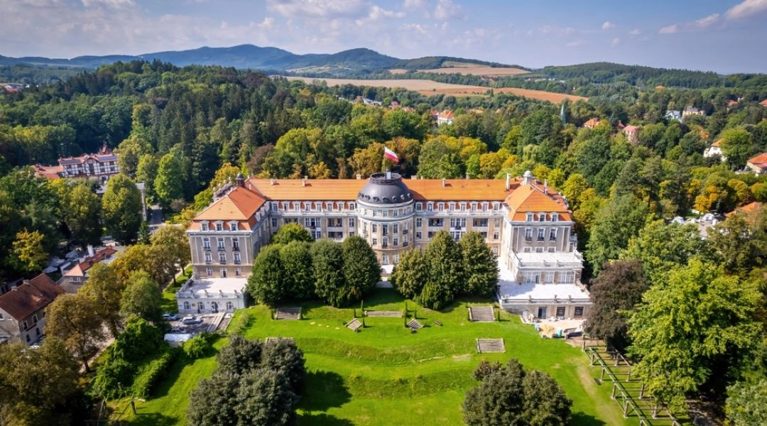 Widok z góry na zabytkowy Dom Zdrojowy w Szczawnie-Zdroju otoczony parkiem i wzgórzami.
