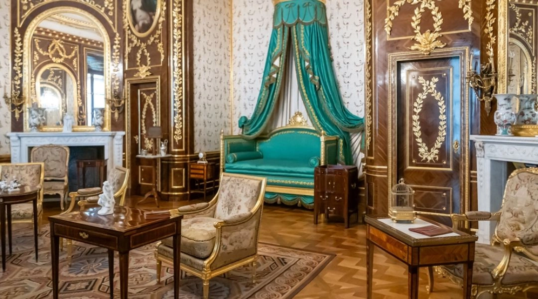Zamek Królewski w Warszawie, eleganckie wnętrze z XVIII wieku, złote zdobienia, kryształowy żyrandol i zielony baldachim nad kanapą.