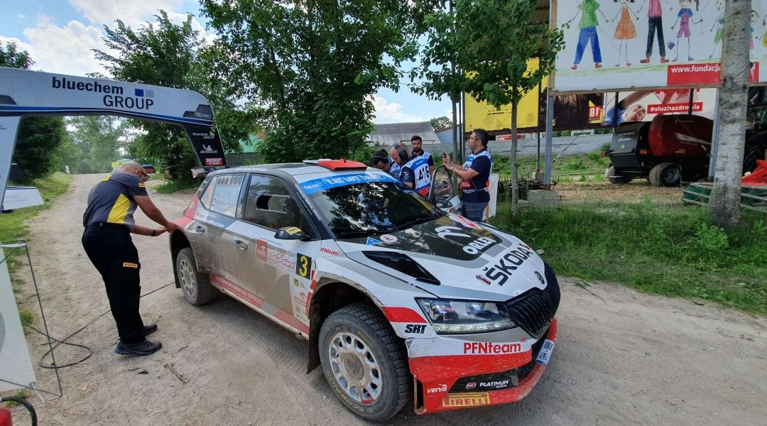 Samochód rajdowy Škoda zatrzymany na punkcie kontroli czasu podczas Rajdu Polski, obok pracują członkowie obsługi.