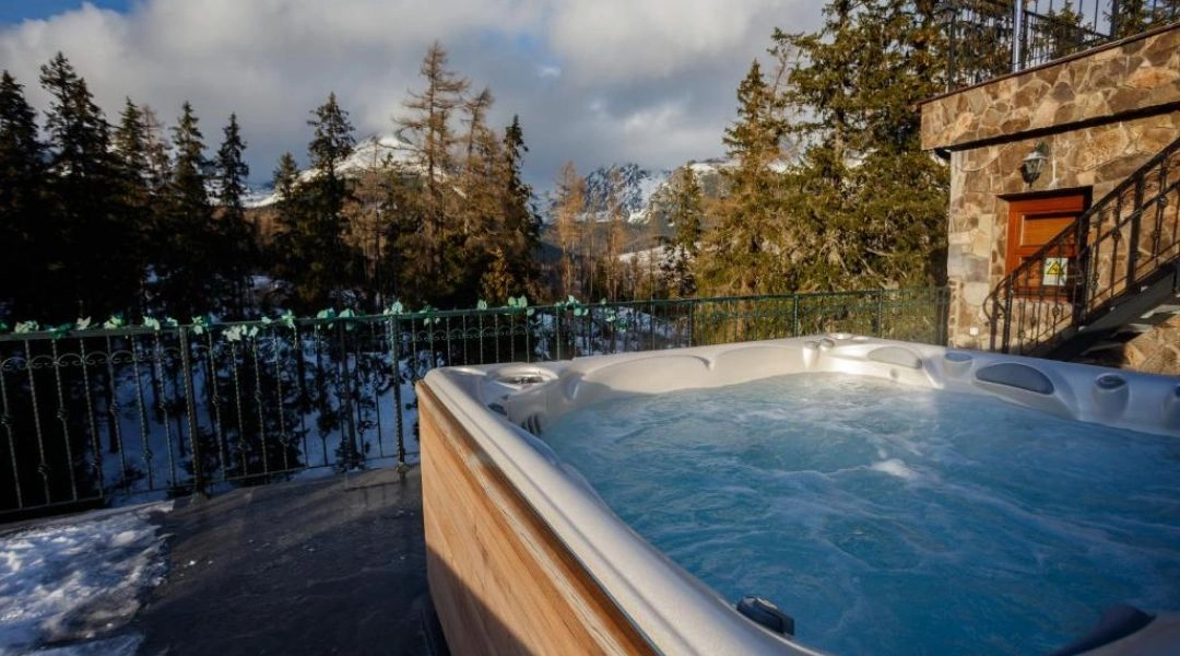 Zewnętrzne jacuzzi na tarasie Hotelu Borovica w Štrbskim Plesie z widokiem na ośnieżone Tatry i otaczający hotel las.