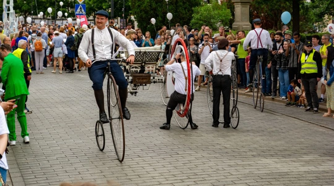 Artyści na retro rowerach jadą Krakowskim Przedmieściem podczas Parady Syrenki.