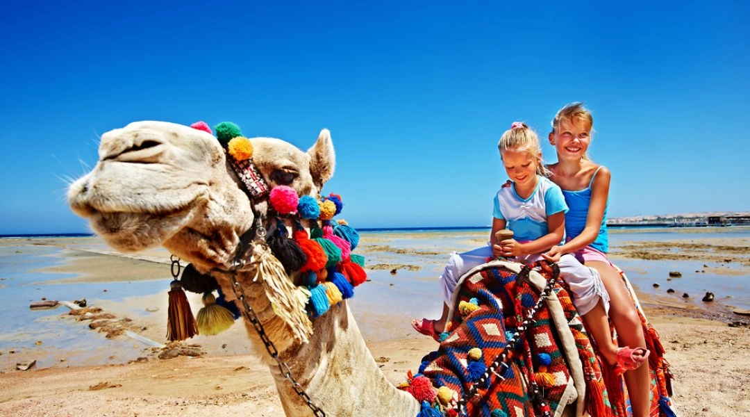 Dwoje dzieci jadących na wielbłądzie na plaży w Egipcie.