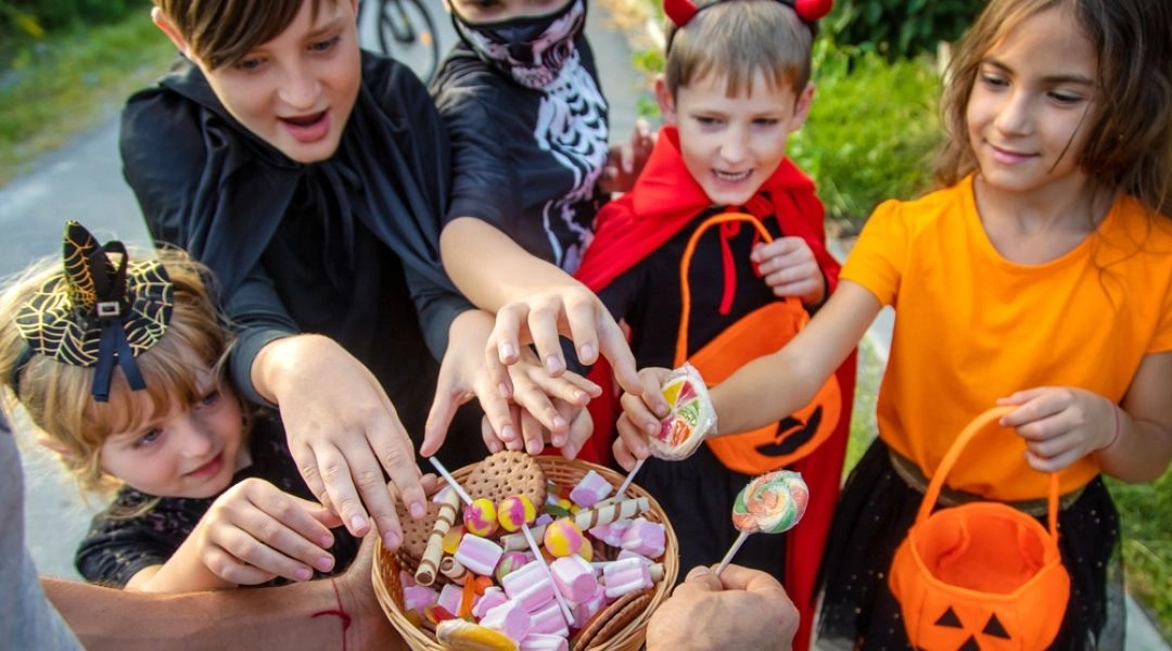Dzieci w halloweenowych przebraniach sięgają po słodycze z wiklinowego koszyka podczas zabawy na świeżym powietrzu.