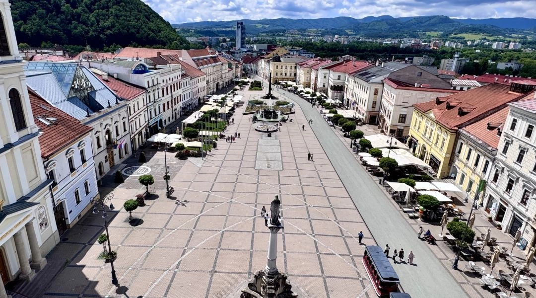 Widok z góry na plac Słowackiego Powstania Narodowego w Bańskiej Bystrzycy, otoczony zabytkowymi kamienicami i kawiarniami.