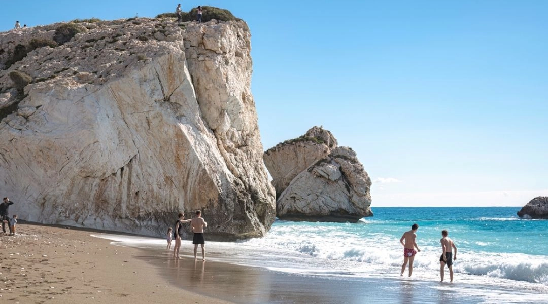Plaża w okolicach Pafos z jasnymi skałami i spacerującymi ludźmi.