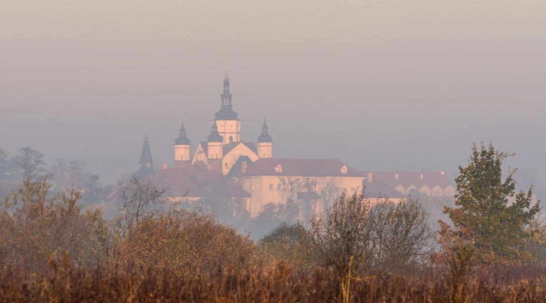 Monastyr w Supraślu widziany z oddali we mgle, ponad łąkami i zaroślami.