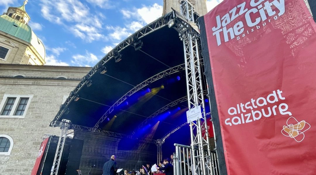 Scena festiwalu Jazz&TheCity Salzburg z czerwonym banerem Altstadt Salzburg i muzykami przygotowującymi się do występu.
