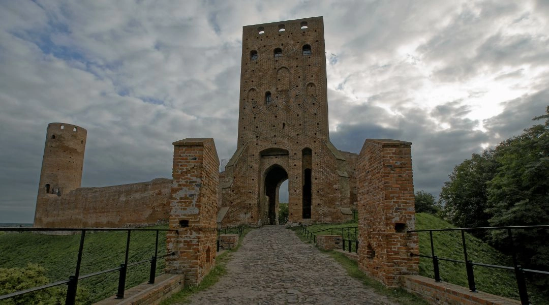 Ceglany zamek w Czersku z wysoką wieżą, kamiennym dojściem i pochmurnym niebem.
