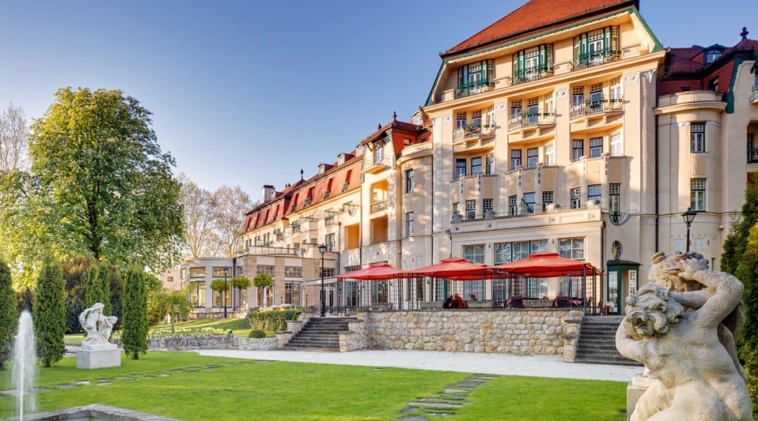 Zabytkowy hotel Thermia Palace w Pieszczanach z tarasem restauracyjnym, ogrodem, fontanną i kamiennymi rzeźbami.