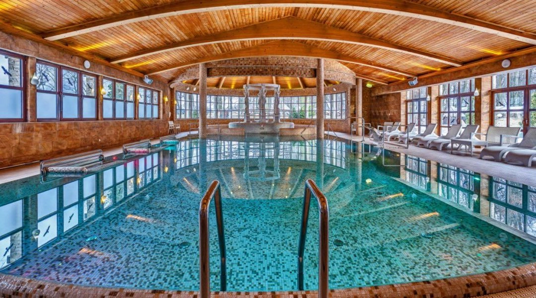 Basen w Manor House SPA w Chlewiskach z drewnianym sufitem i leżakami przy oknach.