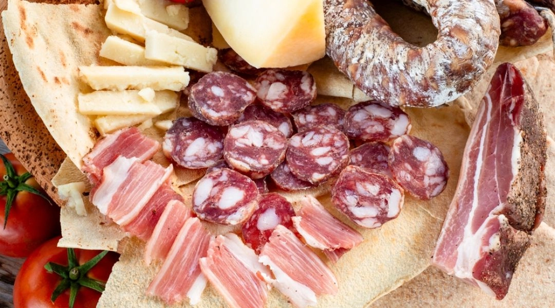 Deska sardyńskich serów, kiełbas i dojrzewających wędlin podanych z pane carasau i pomidorami.