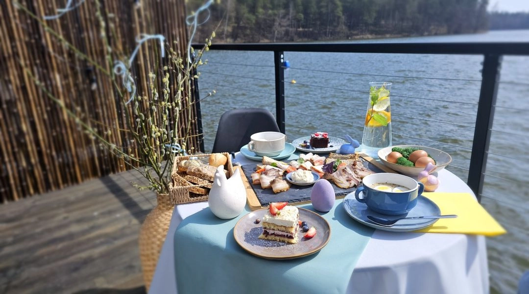 Wielkanocne śniadanie podane na stole na tarasie nad jeziorem, z ciastem, jajkami, pieczywem i dekoracjami.