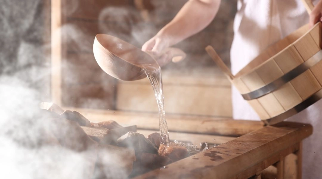 Polewanie kamieni w saunie wodą, rytuał saunowy, para unosząca się nad piecem.