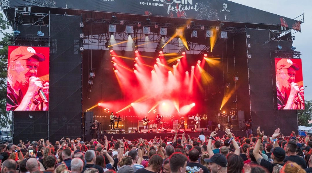 Tłum publiczności przed dużą sceną Jarocin Festival podczas koncertu z czerwonym i żółtym światłem.