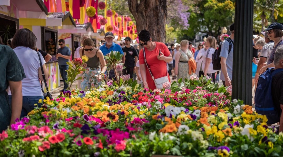 Stoisko z kolorowymi kwiatami na Targu Kwiatowym w Funchal, ludzie oglądają i wybierają rośliny.