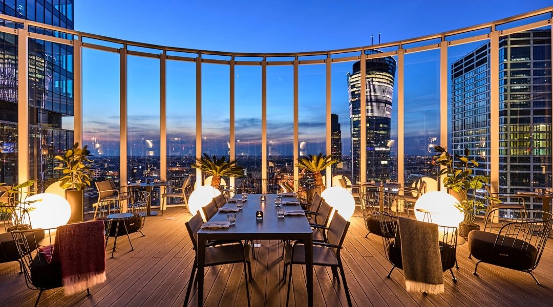 Taras The Roof Skybar w Warszawie z widokiem na biurowce Woli i panoramę miasta po zmroku.