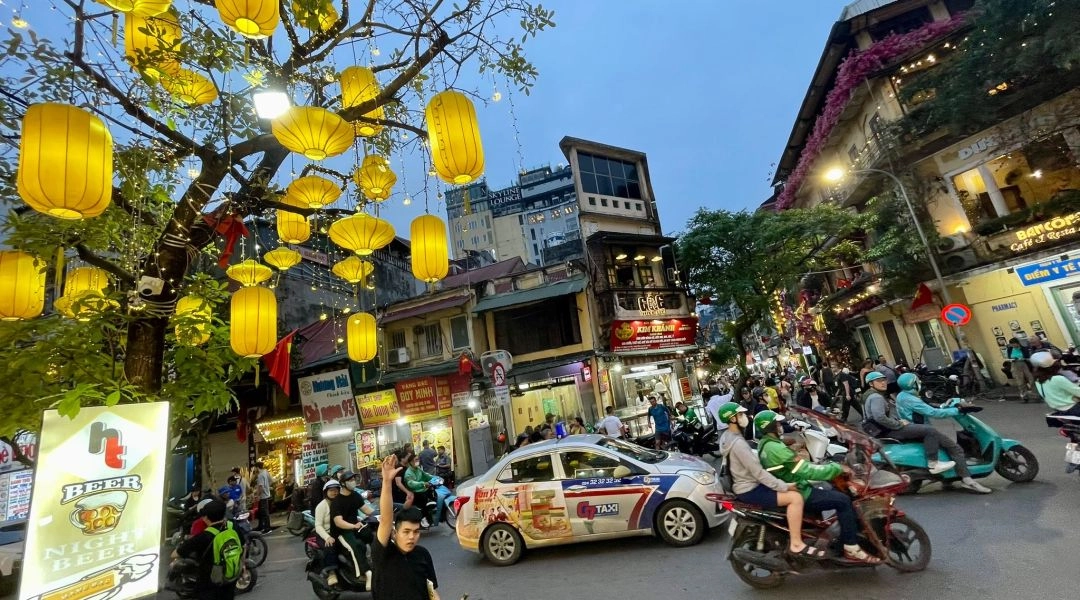 Wieczorna ulica w Hanoi z żółtymi lampionami, skuterami, taksówką i tłumem ludzi
