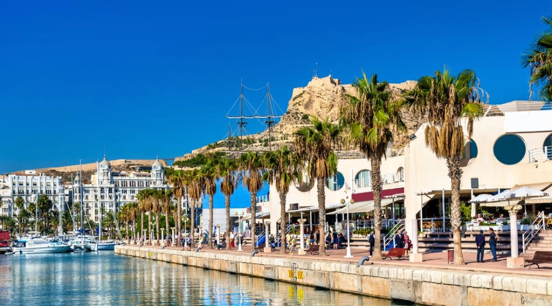 Promenada Explanada de España w Alicante z palmami, kawiarniami i zamkiem św. Barbary na wzgórzu w tle.
