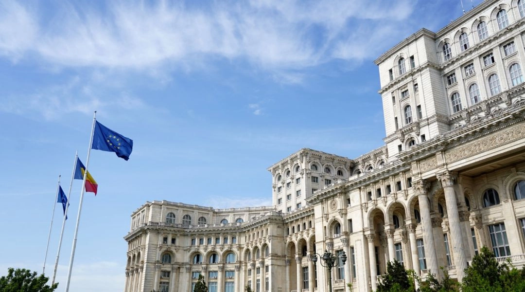 Bogato zdobiona fasada Pałacu Parlamentu w Bukareszcie oraz flagi Rumunii i Unii Europejskiej