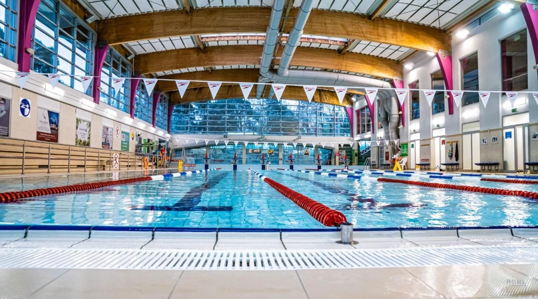 Kryta pływalnia miejska w Warszawie z torami pływackimi i wysokim sufitem.