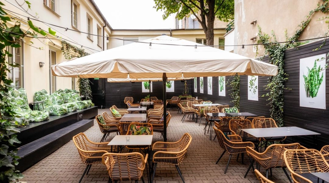 Ogród restauracji Przyjaciele w Warszawie, stoliki pod jasnymi parasolami, wiklinowe krzesła i zielone akcenty na patio.