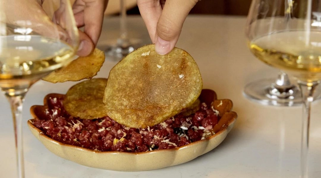 Talerz z tartarem i chipsami oraz kieliszki białego wina na stole w wine barze.
