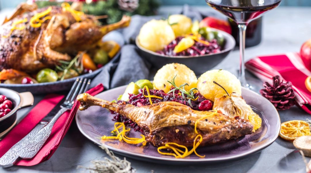 Porcja gęsiny z kapustą i kluskami śląskimi, kieliszek czerwonego wina, świąteczna aranżacja stołu.