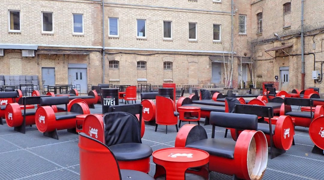 Dziedziniec dawnego więzienia na Łukiszkach w Wilnie z industrialną zabudową i nowym układem miejsc do siedzenia.