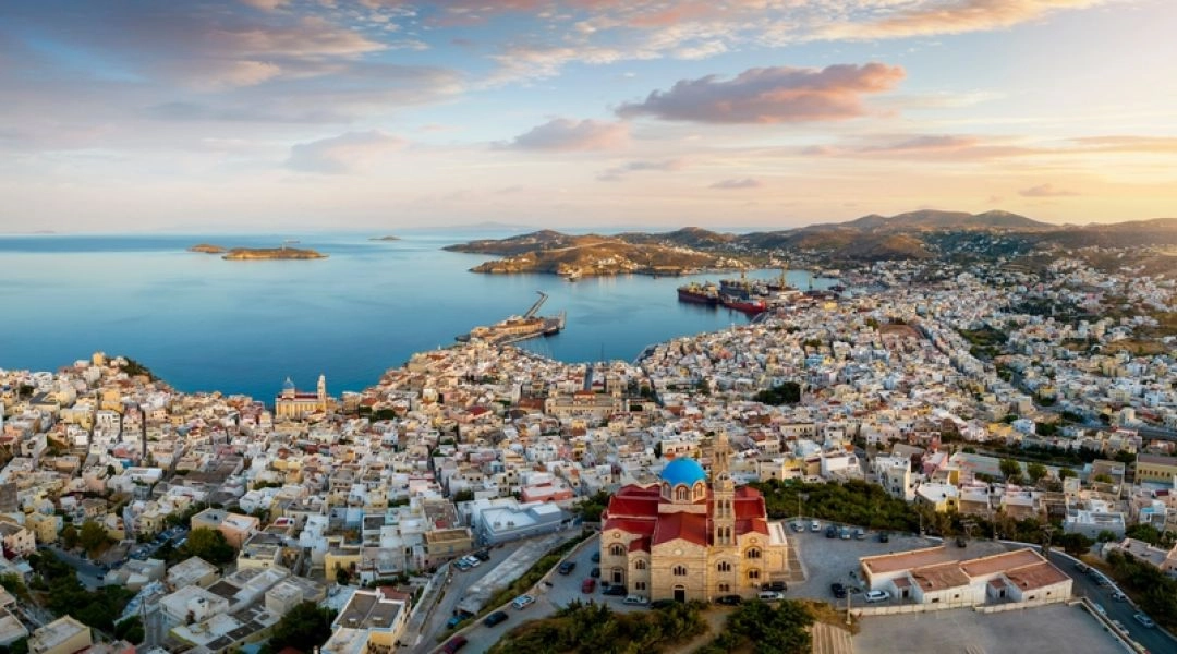Panorama greckiej wyspy Syros z widokiem na Ermupoli, port, zatokę, kościół i białą zabudowę miasta o zachodzie słońca.