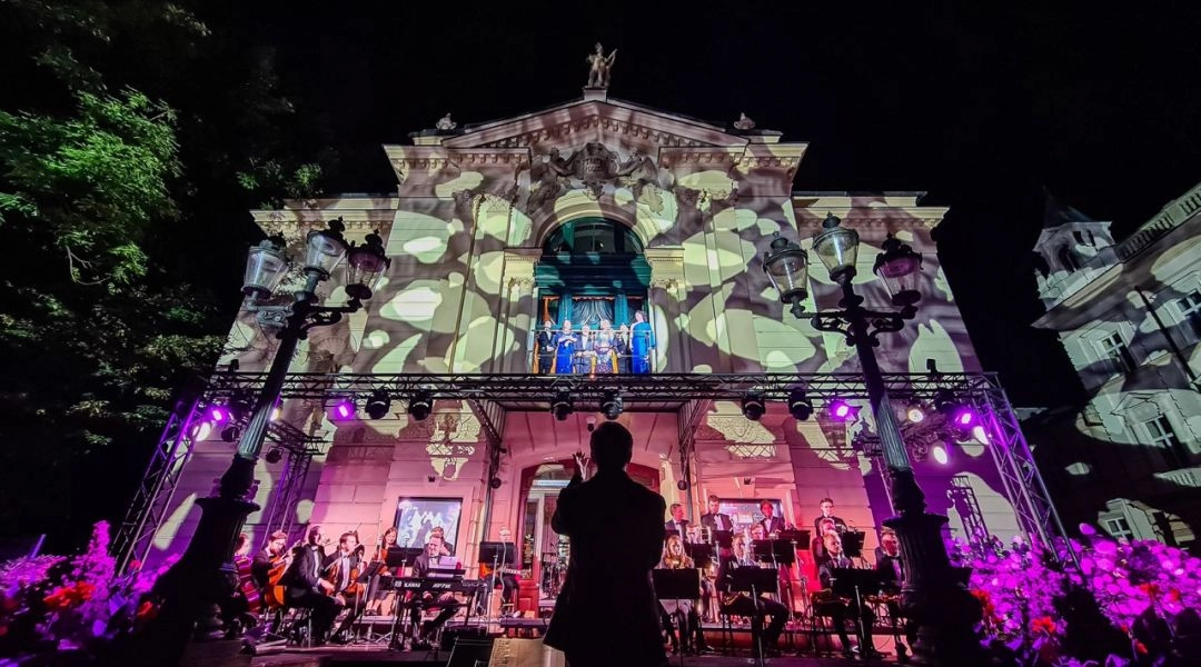 Wieczorny koncert przed podświetlonym gmachem Teatru Polskiego w Bielsku-Białej, z orkiestrą i artystami występującymi w oknie.