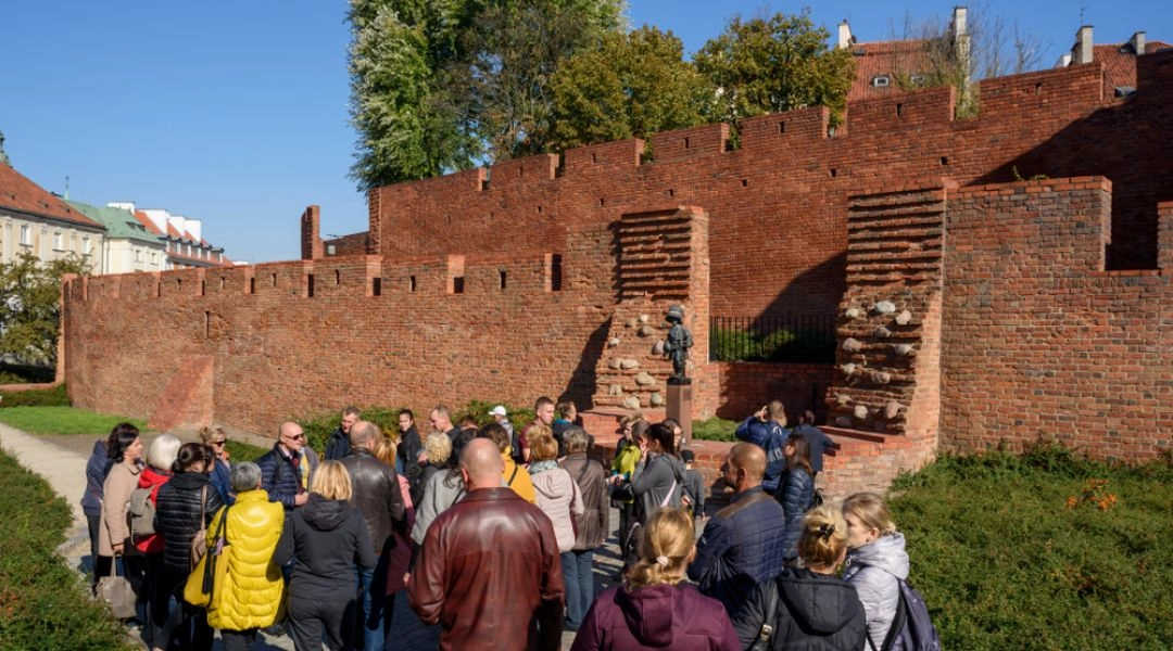 Grupa uczestników podczas spaceru z przewodnikiem przy murach obronnych Starego Miasta w Warszawie
