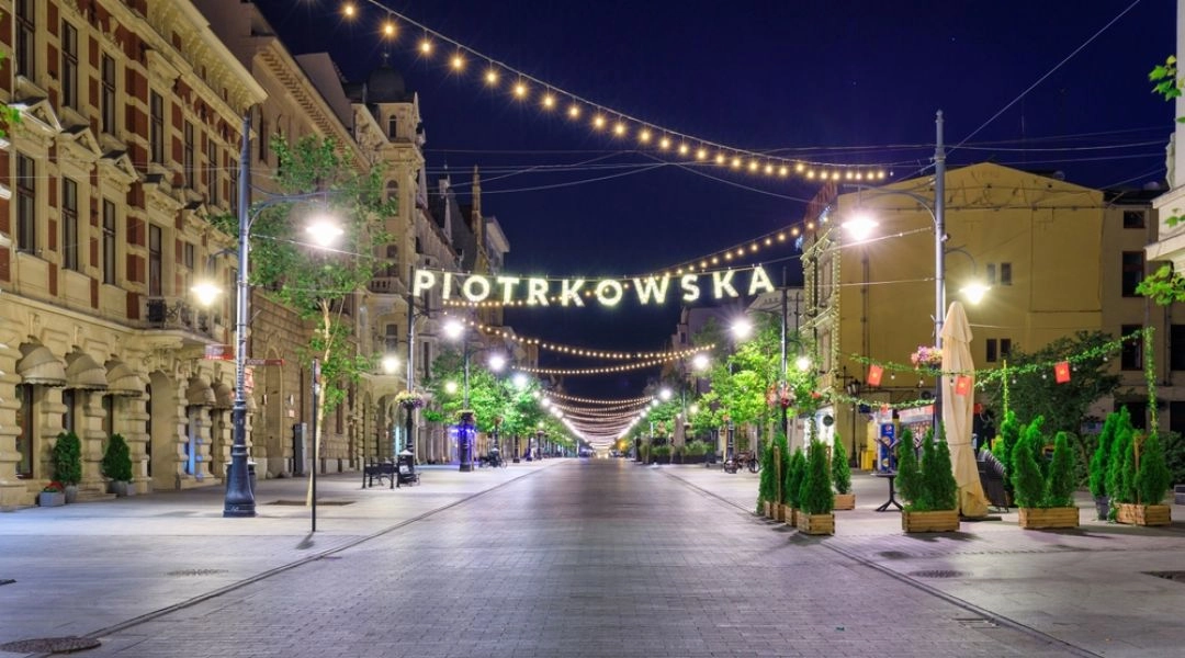 Oświetlona nocą ulica Piotrkowska w Łodzi z zabytkowymi kamienicami i girlandami świateł.