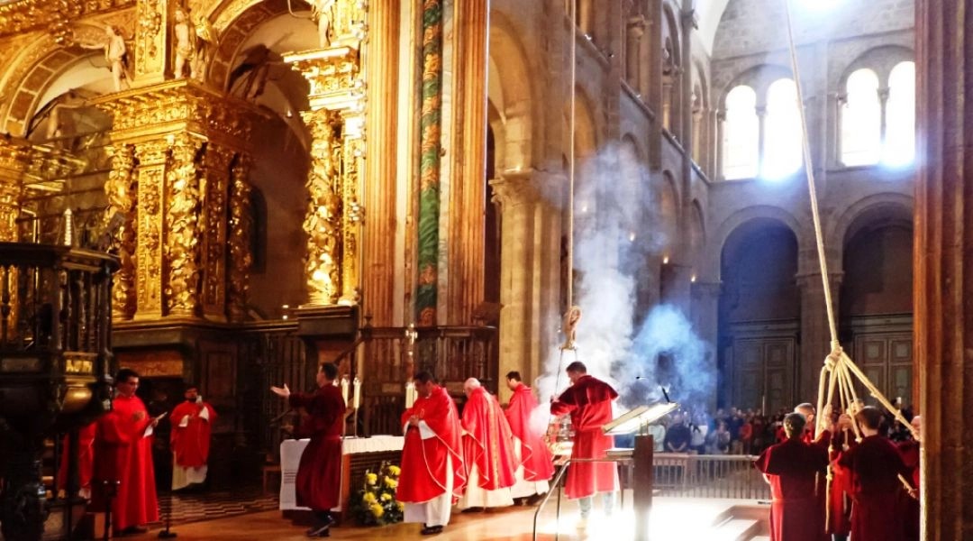 Wnętrze katedry w Santiago de Compostela podczas ceremonii Botafumeiro, kapłani w czerwonych szatach i unoszący się dym.