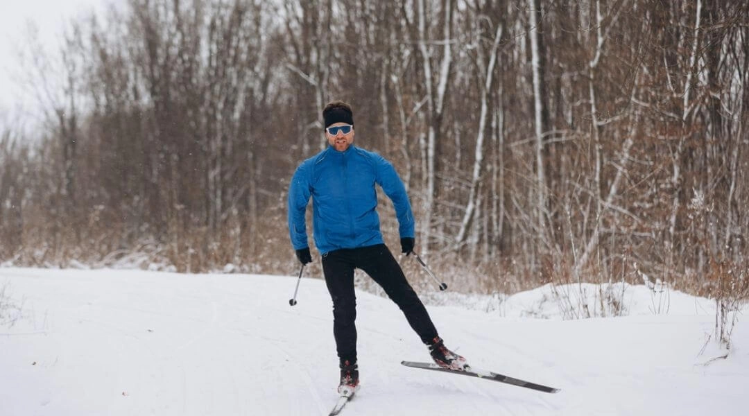 Narciarz na nartach biegowych na zaśnieżonej leśnej drodze w Warszawie zimą.