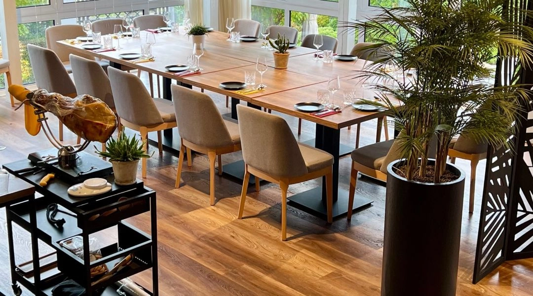 Jasne wnętrze restauracji El Patio w Warszawie, długi drewniany stół, duże okna i widok na zieleń za szybami.