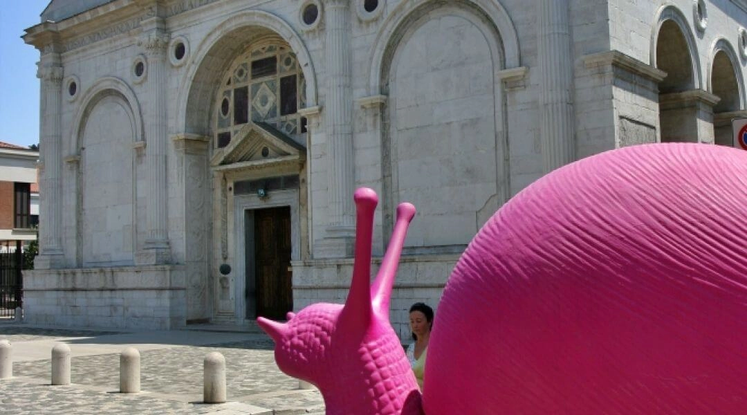 Duża różowa figura ślimaka ustawiona przed zabytkowym kościołem w Rimini podczas Różowej Nocy.