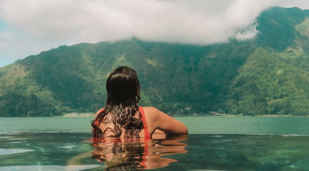 Kobieta w basenie termalnym patrzy na zielone zbocza gór spowite mgłą.