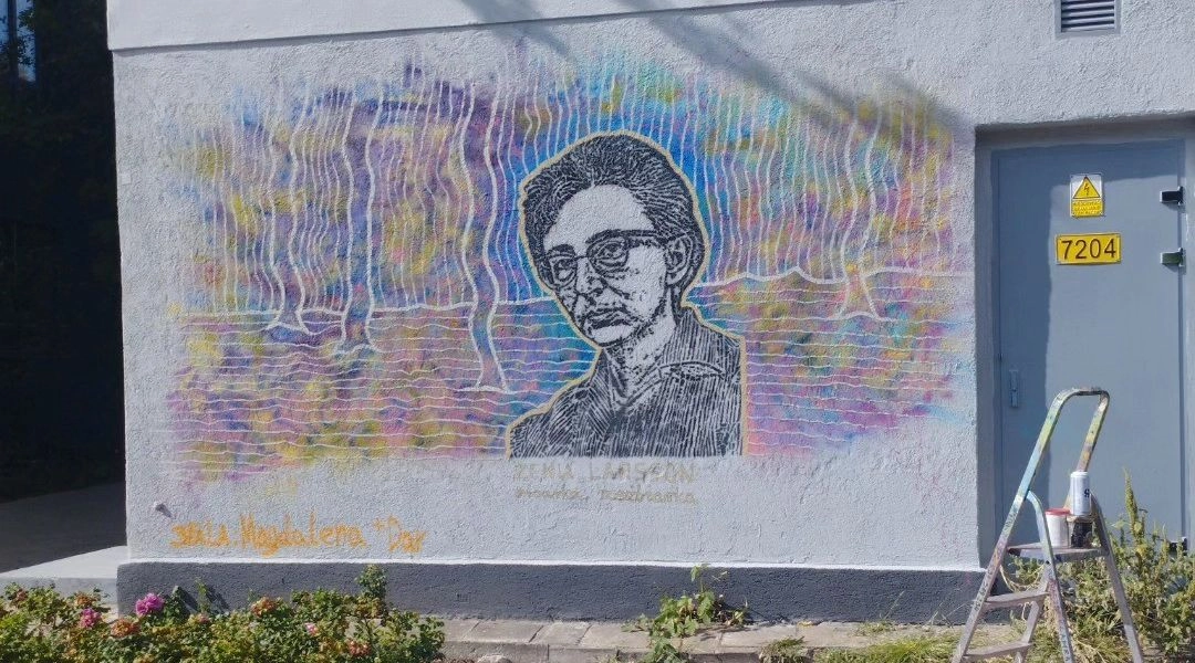 Mural z portretem Zenii Larsson na budynku przy ul. Dzielnej w Warszawie, pastelowe tło i techniczna elewacja transformatora.