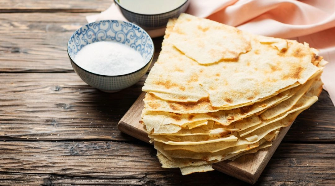 Cienki, chrupiący chleb pane carasau podany z oliwą i solą na drewnianym stole.