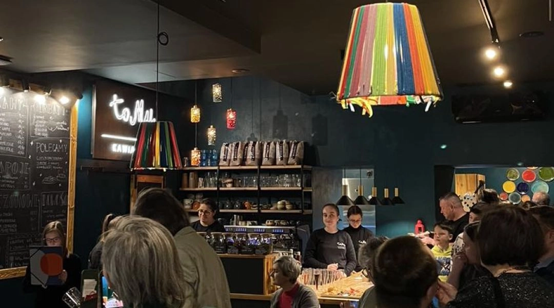 Wnętrze kawiarni toMy w Warszawie z gośćmi przy barze i kolorową lampą nad stolikiem.