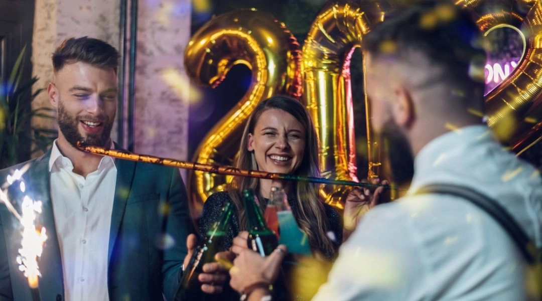 Grupa młodych osób świętująca sylwestra, z balonami 2026 w tle i zimnymi ogniami w rękach.